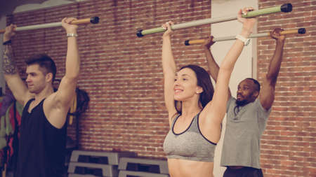 Diverse group of fit young people exercising with bars in gym