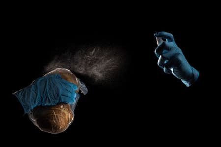 Hands in protective gloves desinfecting bread on black studio background