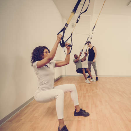 Group of young fit multinational training with straps in modern fitness club