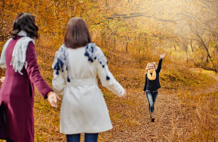 Two young women in autumn park greeting their girlfriend and keeping distance, getting rid of the autumn desiresの写真素材