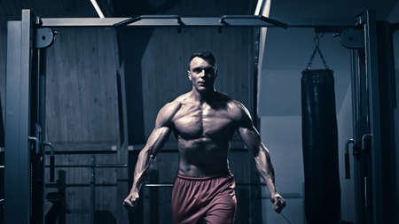 Young handsome sporty bodybuilder exercising with stretching band in gym