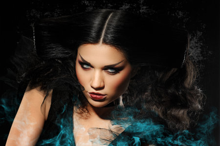 Young stylish female brunette with creative makeup for Halloween party with blue smokeの写真素材