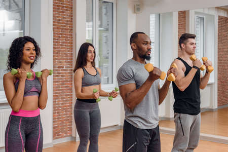 Multiethnic group of fit young people training in gym and lifting dumbbells