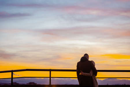 Back view of young couple in love watching sunset together during weekendの写真素材