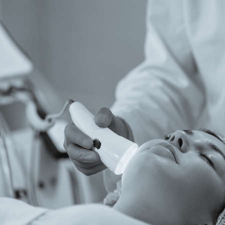 Woman having color light therapy to stimulate facial skin wellbeing.black and white image with blue...