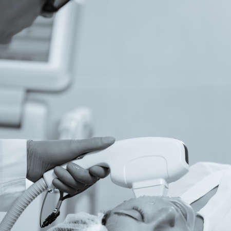 Woman receiving face skin phototherapy procedure in clinic of aesthetic cosmetology. black and white...