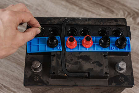 Closeup photo of auto mechanic checking car battery, unscrewing the lid with a coin