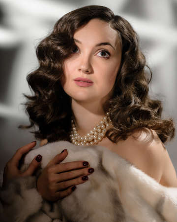 Portrait of luxury fashion woman in fur coat and pearls showing shoulderの写真素材