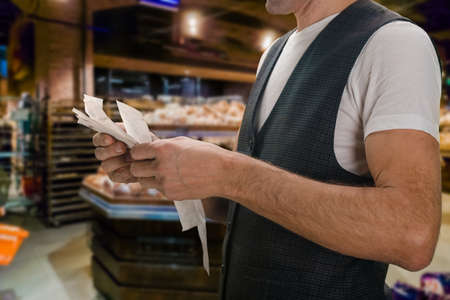 Closeup of young man holding bill to check the price in supermarketの写真素材
