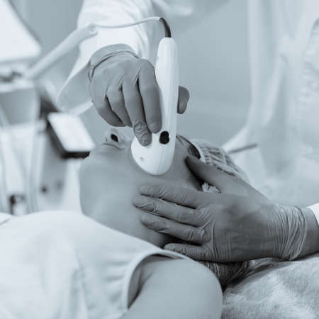 Woman having color light therapy to stimulate facial skin wellbeing. black and white image with blue...