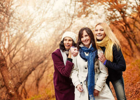 Three attractive happy women walking together in autumn parkの写真素材
