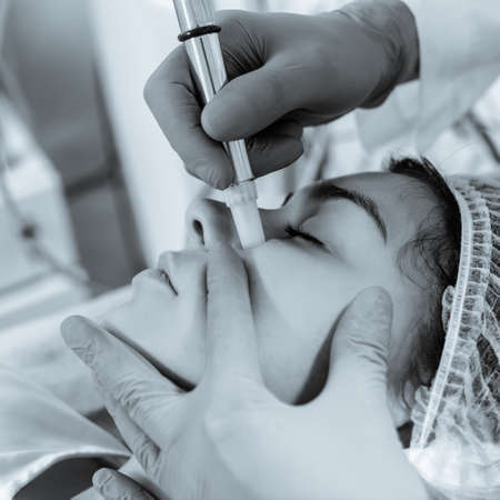 Cosmetologist doing microdermabrasion procedure for woman to refresh her skin tone. black and white...