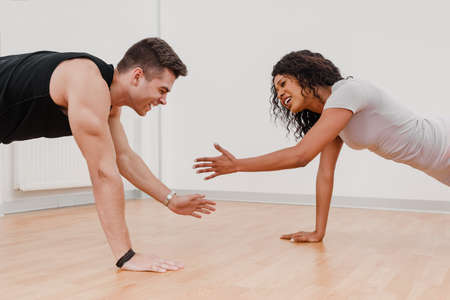 Athletic muscular man and fit mix-raced woman doing plank and shaking handsの写真素材