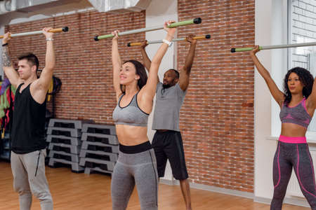 Diverse group of fit young people exercising with bars in gym