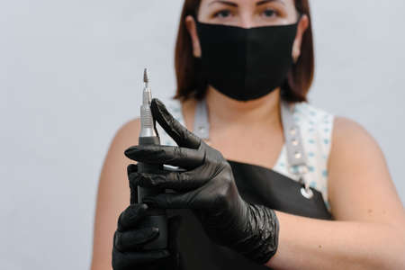 Portrait of woman manicurist showing electric file drill machine in beauty salon