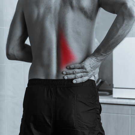 Monochrome photo of muscular man holding his aching back with hand