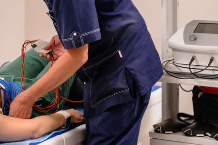 Dnepr, Ukraine- July 17, 2020: Male therapist positioning electrodes on patients body for electro stimblation procedureのeditorial素材