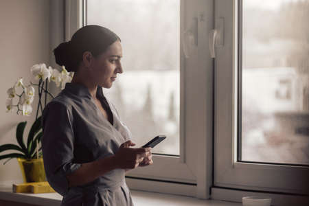 Beautiful young lady in medical uniform resting after work and chatting in smartphoneの写真素材
