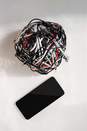 Modern mobile phone with messy bunch of different cables, future progress of wireless technology
