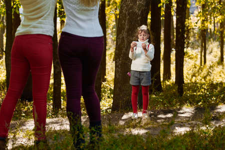 Little cute girl photographing her sisters on smartphone in forestの写真素材