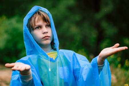 Young boy tourist hiker in blue raincoat enjoying warm summer rainの写真素材