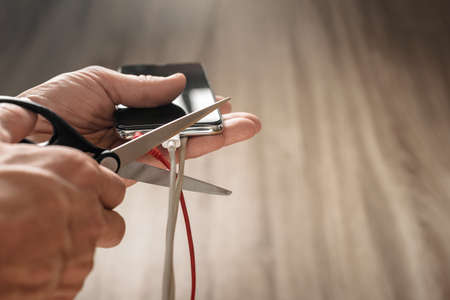Closeup photo of mans hand with scissors cutting smartphone usb wireの写真素材