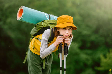 Portrait of tired young boy with backpack and equipment hiking on beautiful summer day in mountains