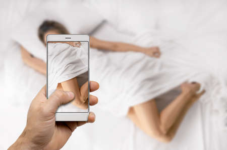 man hand making photo or video using mobile phone while girl lying on bed at homeの写真素材