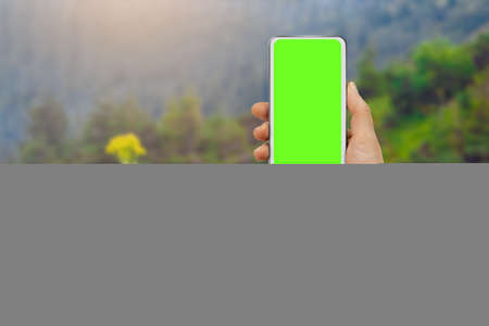 Male hand holding modern mobile phone with green display on the background of forestの写真素材