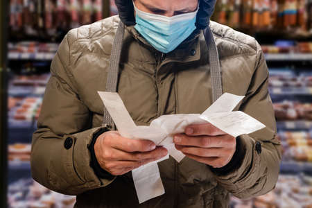 Upset man in supermarket checking grocery bill durind covid-19 epidemicの写真素材