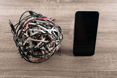 Tangled roll of usb cables and mobile phone on wooden backgroundの写真素材