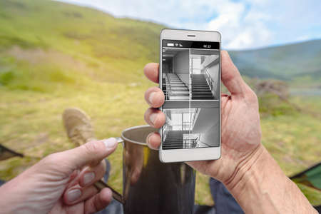 Man resting in mountain and watching cctv home video on smartphoneの写真素材