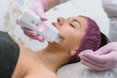 Cosmetologist doing ultrasound rejuvenation procedure to female client in modern beauty salon