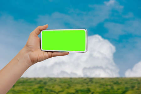 Female tourist holding mobile phone with green chromakey screen against blue sky for mockupの写真素材