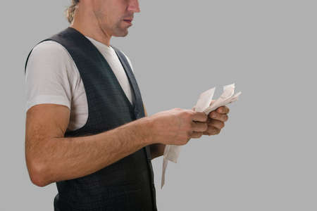 Young man holding supermarket receipt with food purchases on gray background