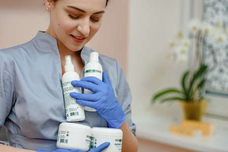 Dnepr, Ukraine- April 20, 2021: Portrait of female cosmetologist in uniform holding a lot of moisturizing and beauty care creamsのeditorial素材