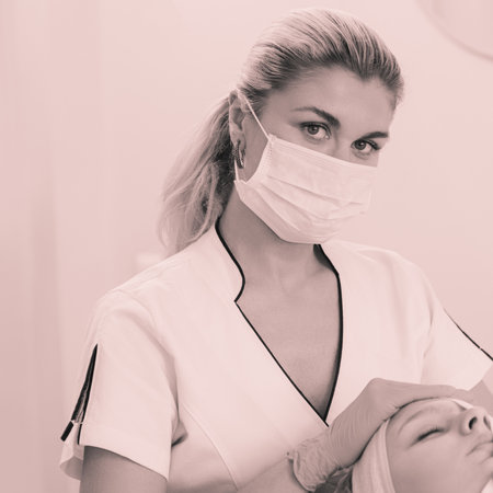Cosmetologist cleaning young woman face with napkin in beauty salon, monochrome image with toningの写真素材