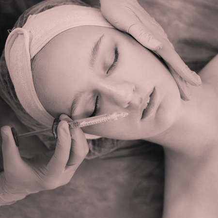 Beautician doctor hands doing beauty procedure to female face with syringe, monochrome image with toningの写真素材