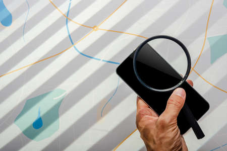Detective hand holding magnifying glass and smartphone in front of city map