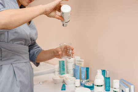 Dnepr, Ukraine- April 20, 2021: Professional beautician pouring moisturizing lotion in glass jar before procedureのeditorial素材