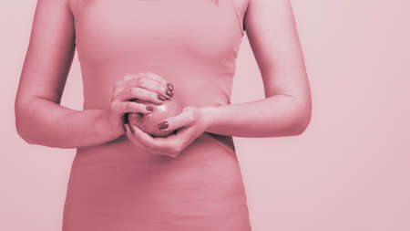 Closeup photo of slim healthy woman holding apple on gray background, monochrome image with pink...