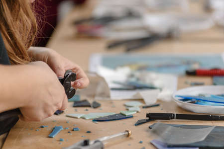 Closeup photo of female hands cutting off piece of glass for mosaic