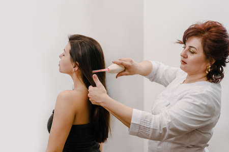 Professional beautician doing darsonval hair treatment procedure for young womanの写真素材