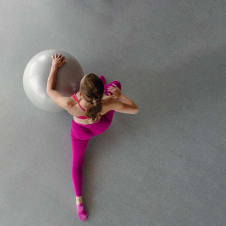 Active strong woman in pink sportswear doing fitness workout with fitball, top view photoの写真素材