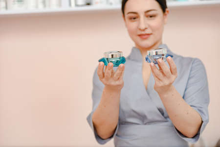 Portrait of young professional woman beautician holding bottles with body cream