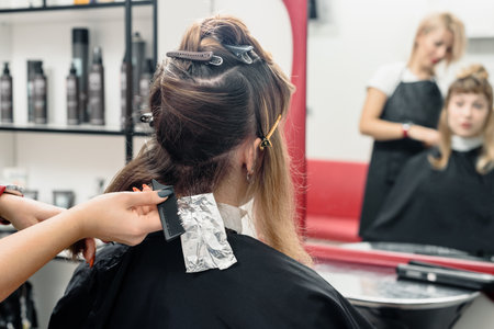 Female stylist putting coloring foils on woman hair in modern beauty salonの写真素材