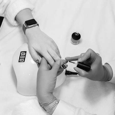 Manicure master in rubber gloves doing gel polish design for female client, black and white imageの写真素材