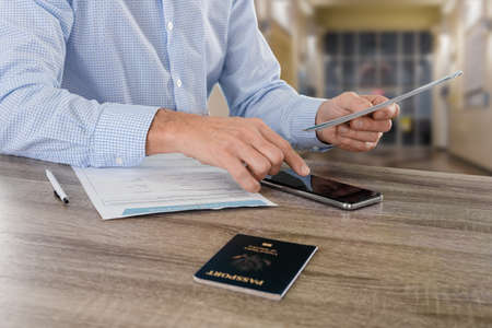Male businessman with smartphone and american passport signing travel insurance form