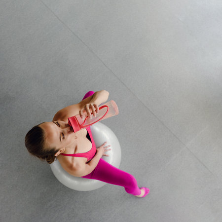 Top view of sportswoman drinking water and using fit ball for training in gymの写真素材