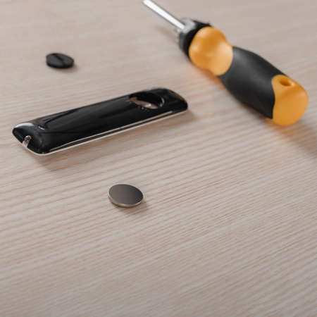 Closeup photo of remote control, battery and screwdriver on wooden table